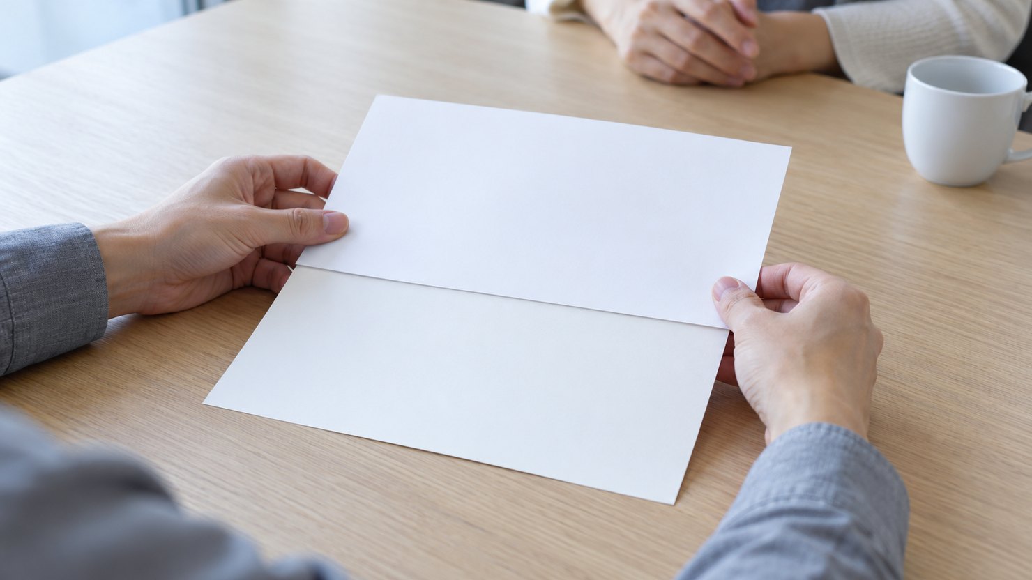 打ち合わせ机で、無地の書類の上半分を白い紙で覆って相手に向ける