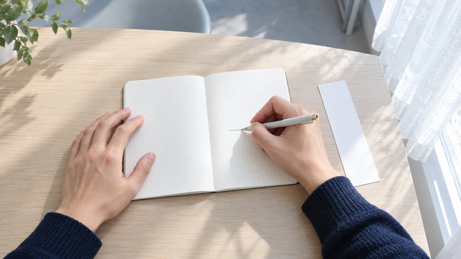 明るい机で、無地の方眼の手帳に短い線を書き、横に無地の細長い紙片を置く