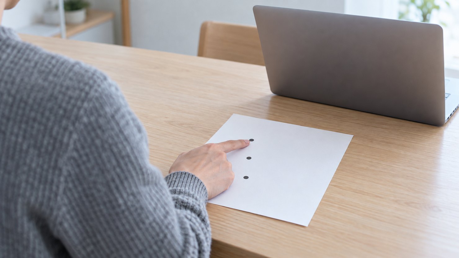 明るい部屋で、ノートパソコンに向かうエンジニアの肩越しに、無地のメモに縦に並ぶ3つの点の1つ目を指で押さえる様子